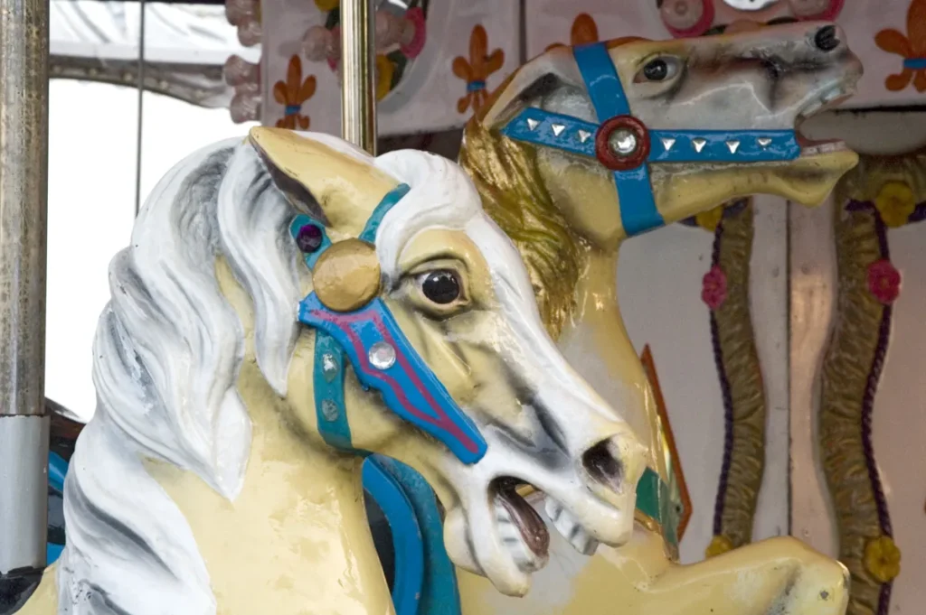 Two painted carousel horses have blue bridles, gold trim, and detailed faces.