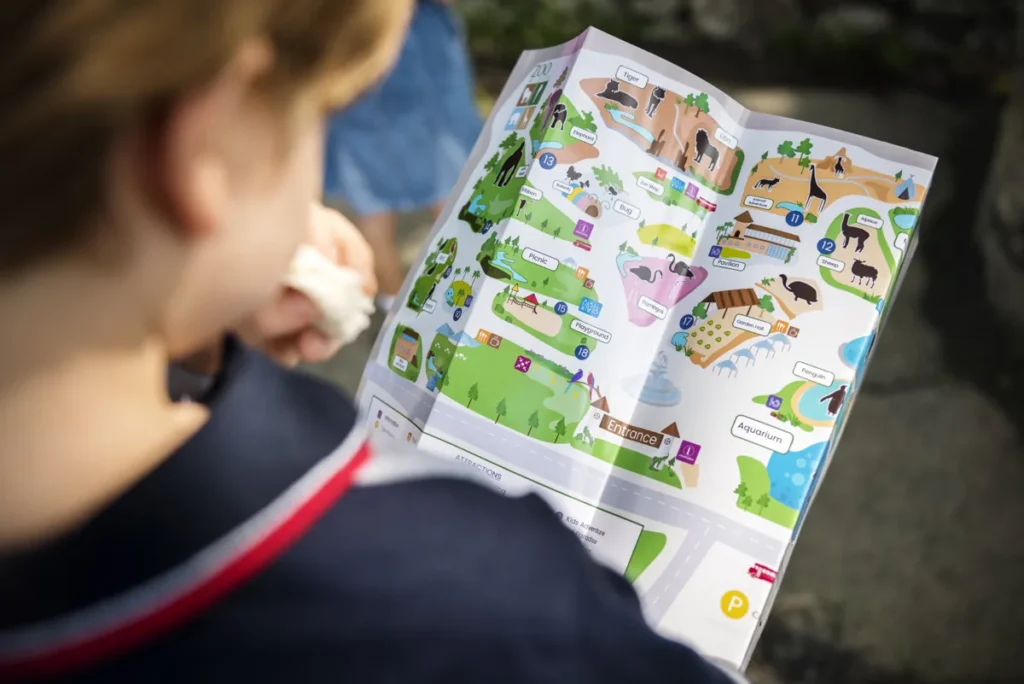 A child looks down at an illustrated zoo map with paths and animal exhibits.