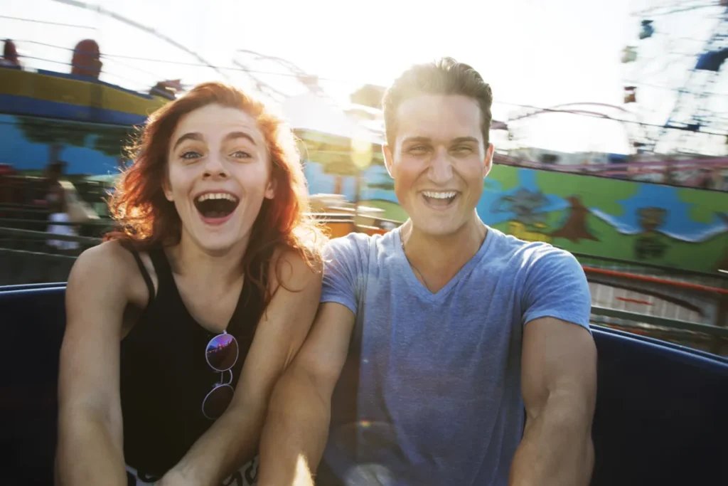 A smiling couple shares a carnival ride as the sun sets behind them.