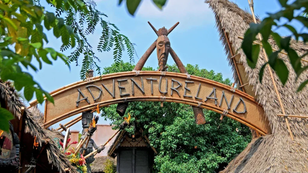 The wooden Adventureland entrance sign is framed by tropical greenery at Disneyland Park.