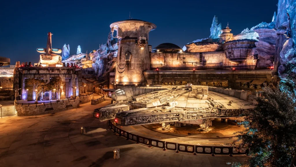 The Millennium Falcon rests beneath Batuu’s illuminated rock spires at night.