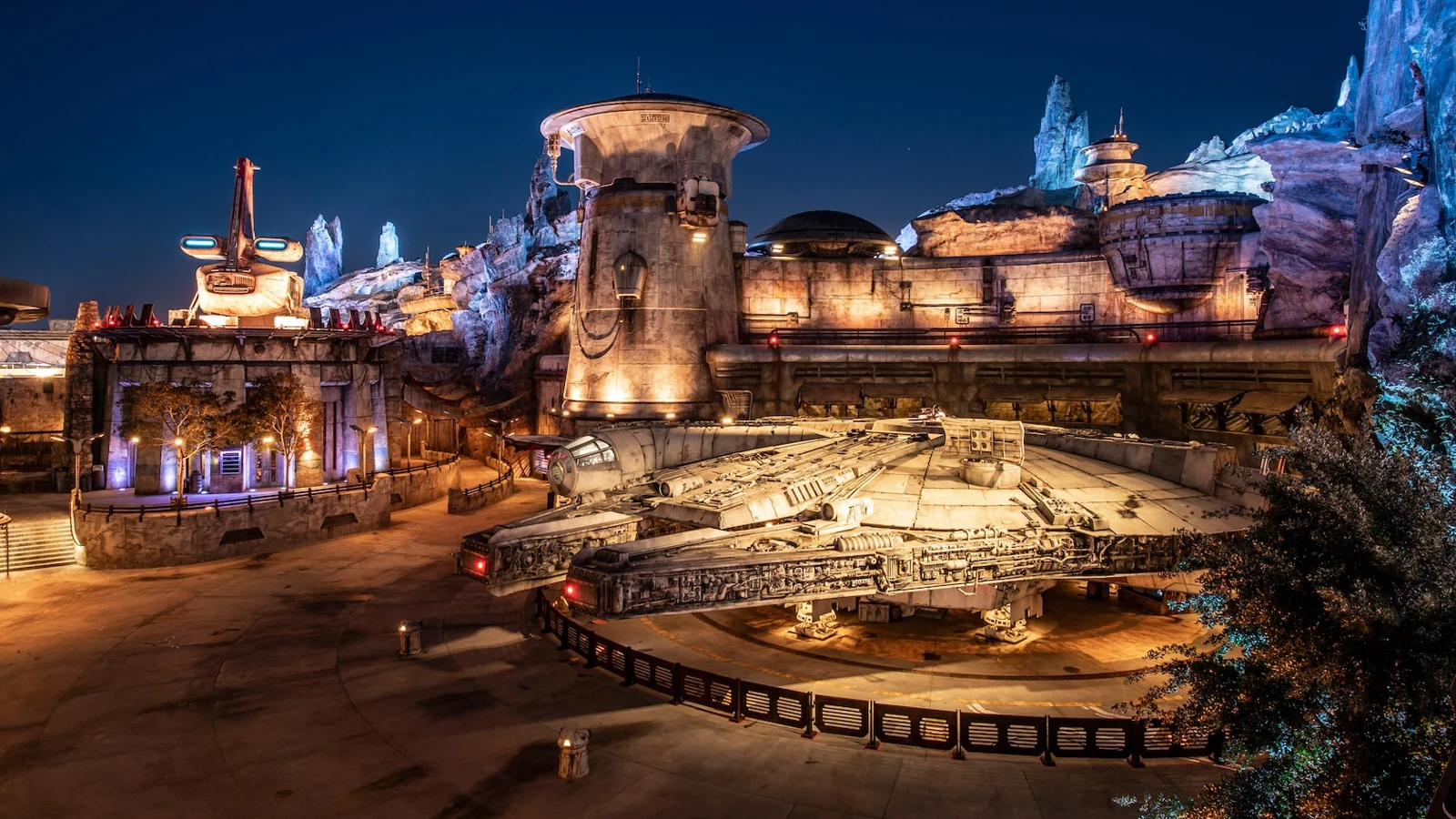 The Millennium Falcon rests beneath Batuu’s illuminated rock spires at night.