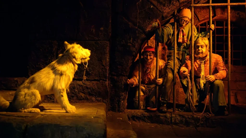 Three pirates behind jail bars reach toward a dog holding a ring of keys in Pirates of the Caribbean.