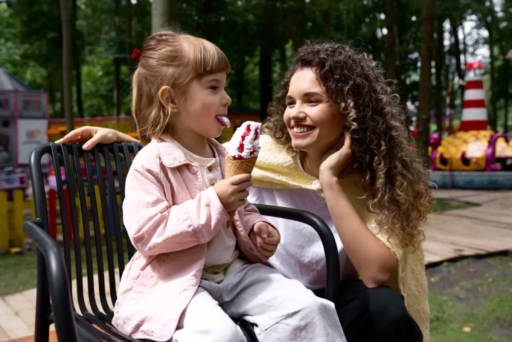 A woman and a girl hold ice-cream cones beside a park bench.
