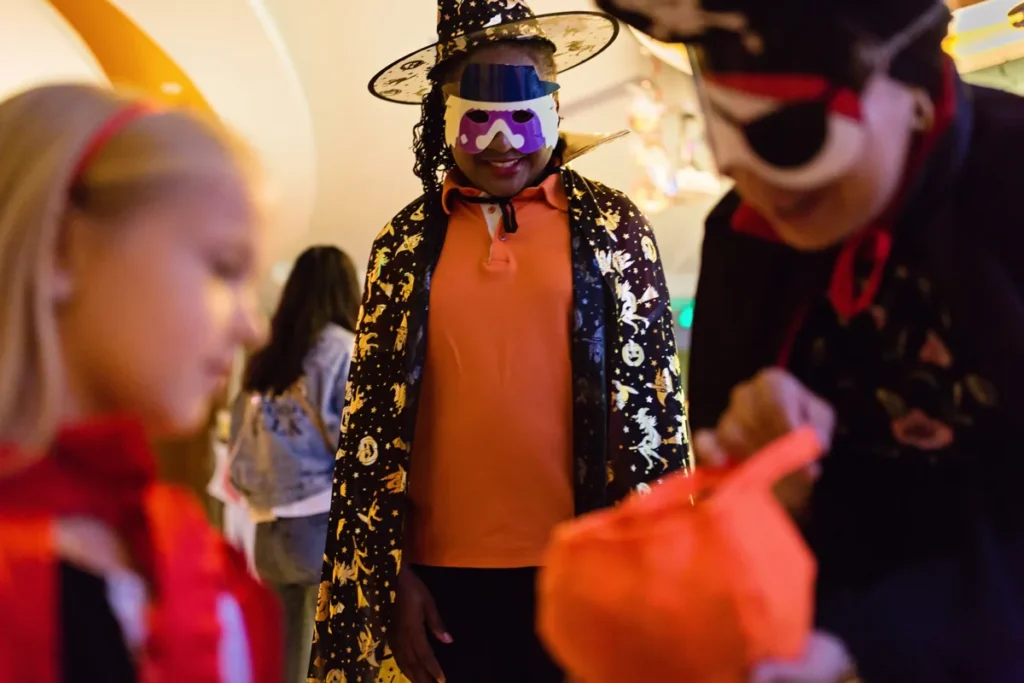 Adults and children wear colorful Halloween costumes and masks at an indoor celebration.