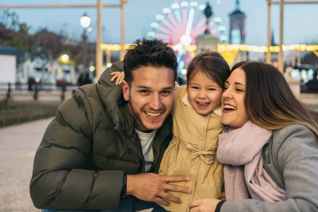 Two adults and a child smile together with fairground rides behind them.