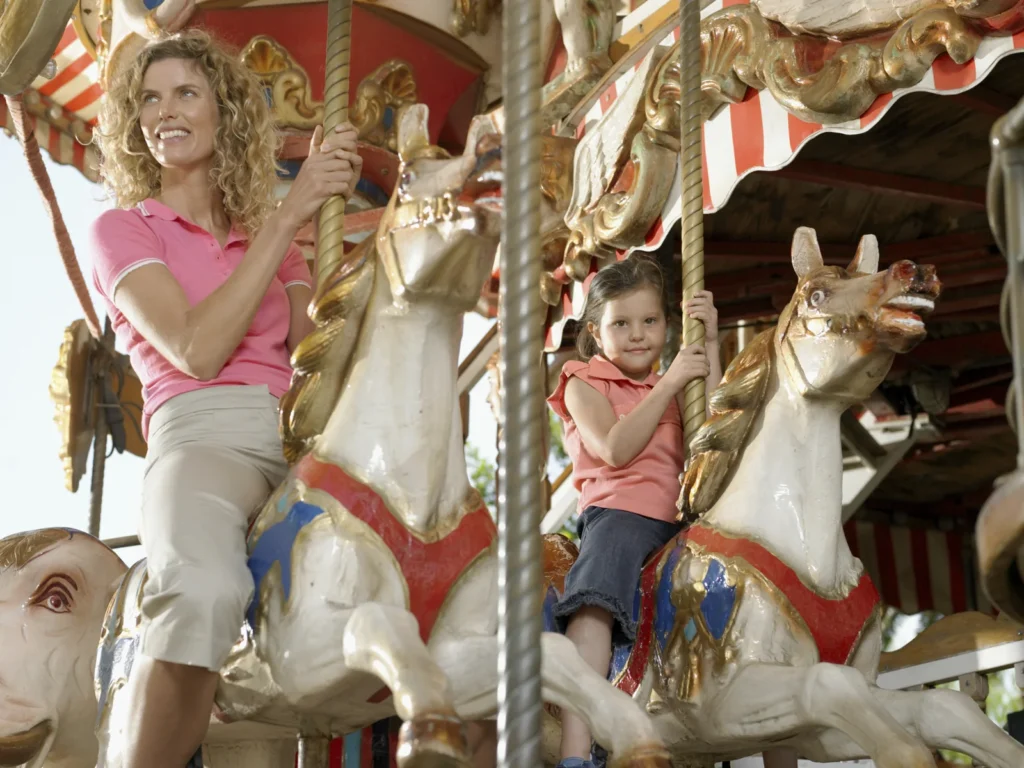 A woman and a child sit on ornate carousel horses.
