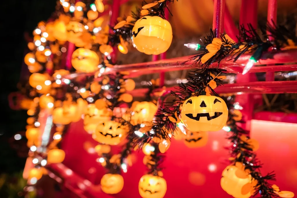 Strings of glowing jack-o’-lantern decorations hang against a warm red background.