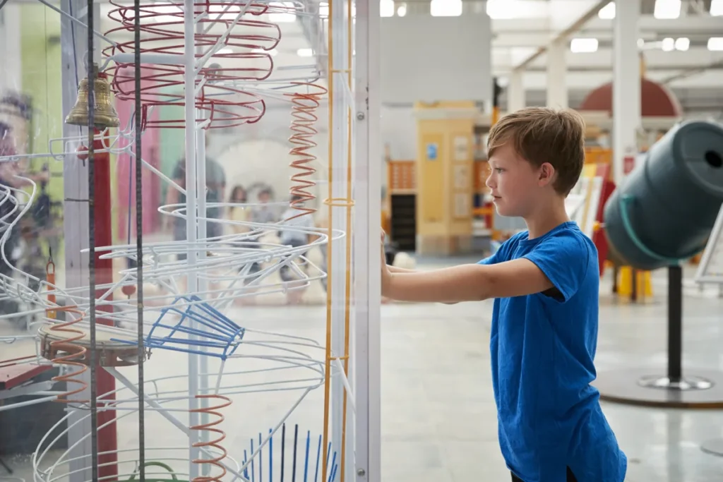 A boy uses an interactive display with spiraling tracks inside a bright science museum.