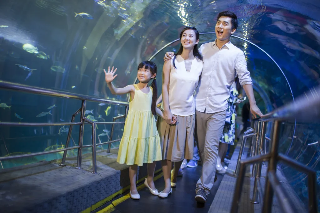 Two adults and a child look at fish while walking through a blue underwater aquarium tunnel.