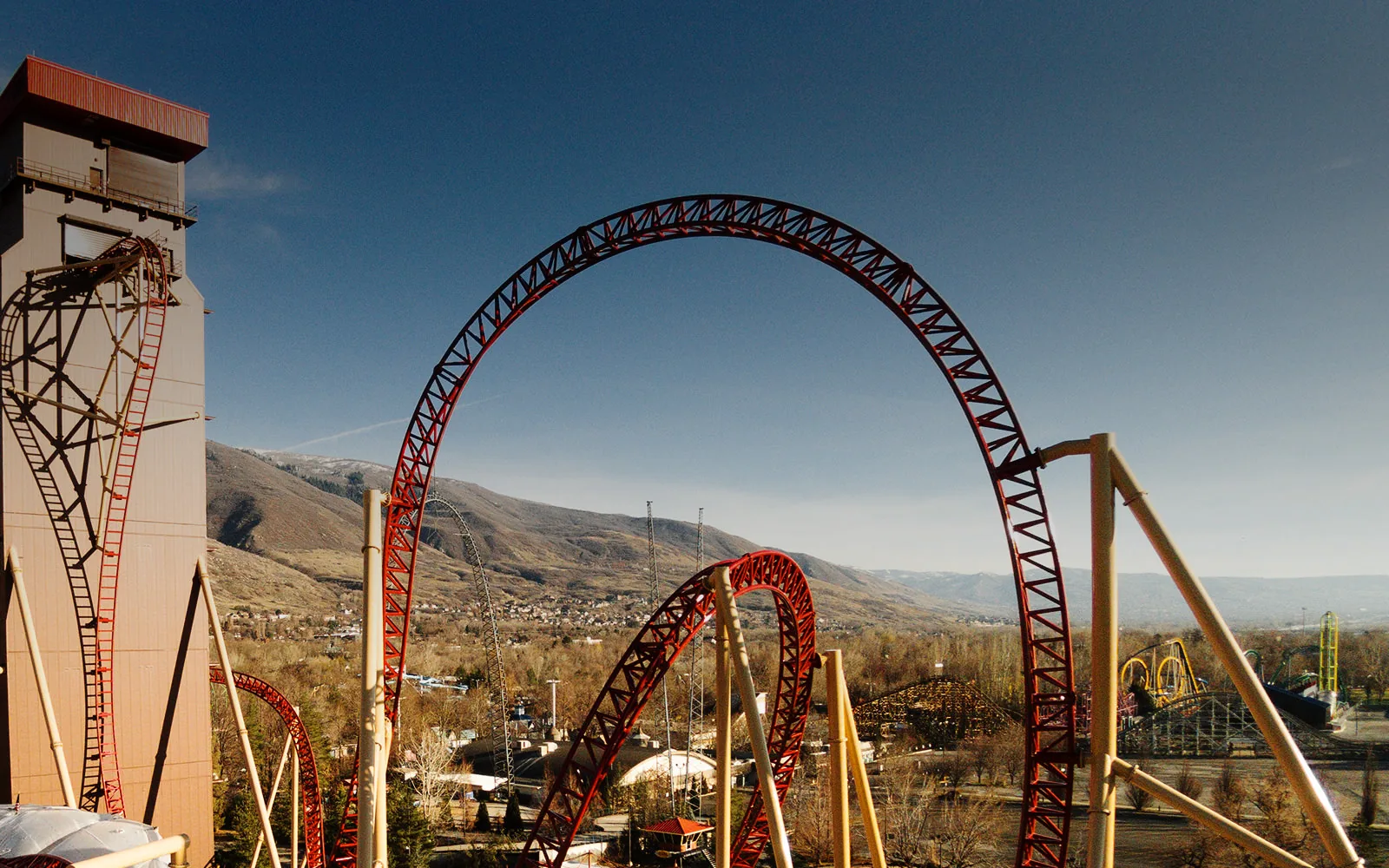Cannibal’s red coaster track rises beside its tower at Lagoon, with Farmington and the Wasatch foothills beyond.