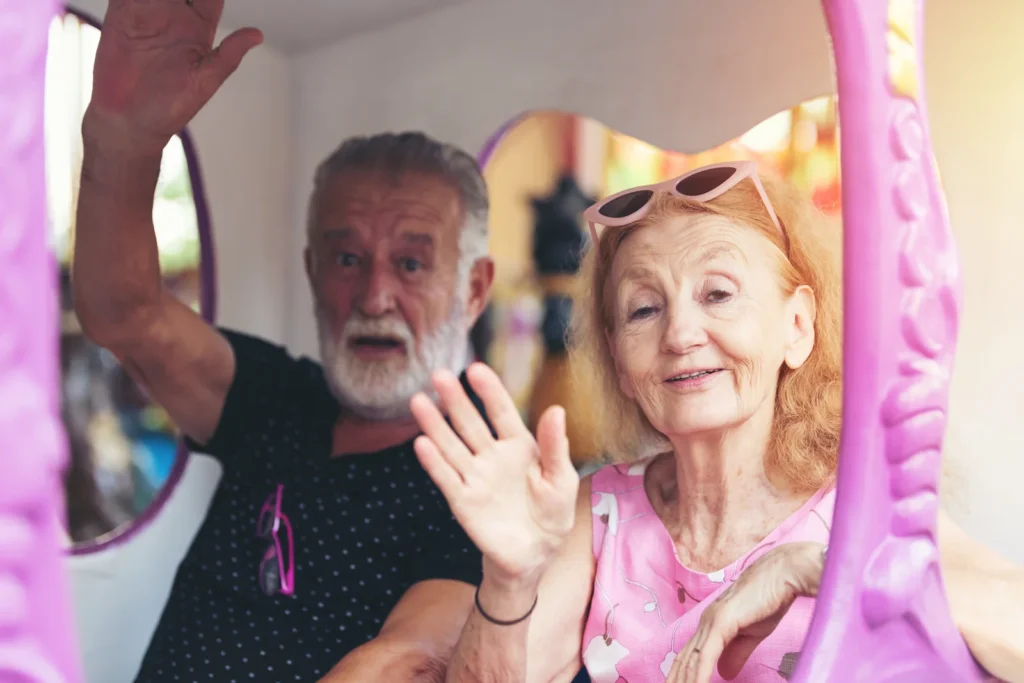 Two older adults wave from a colorful amusement-ride carriage.