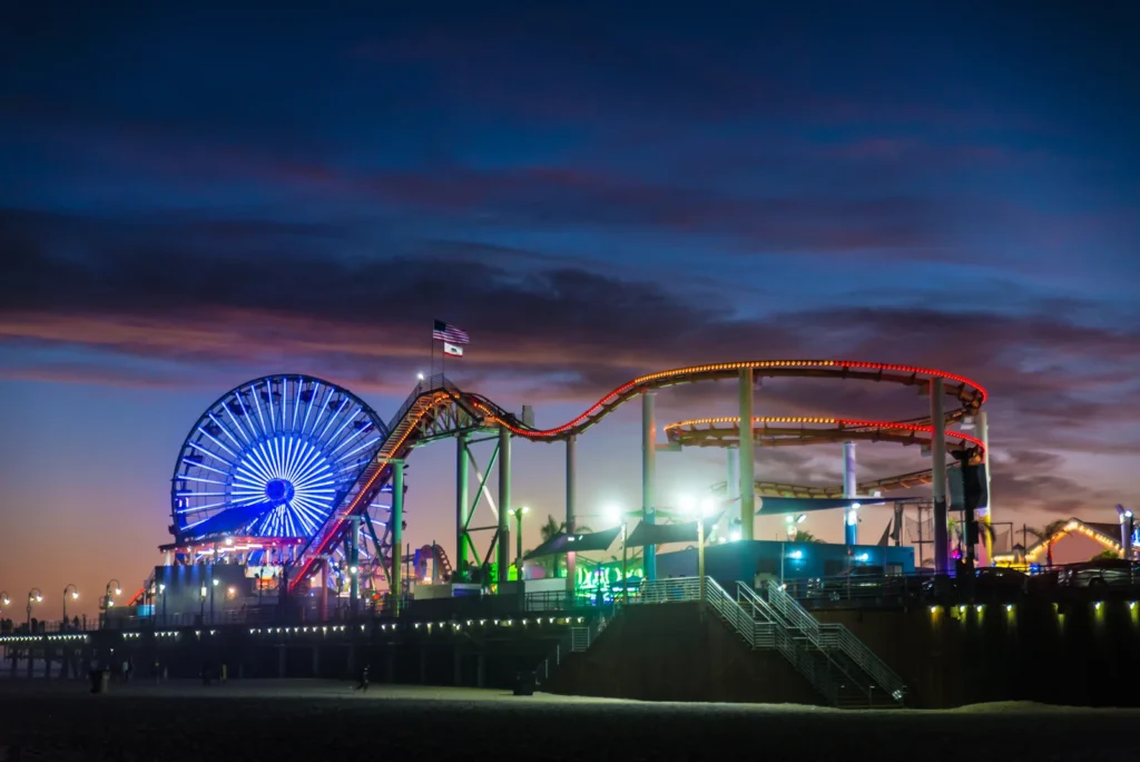 A roller coaster and Ferris wheel light up Santa Monica’s boardwalk at twilight.