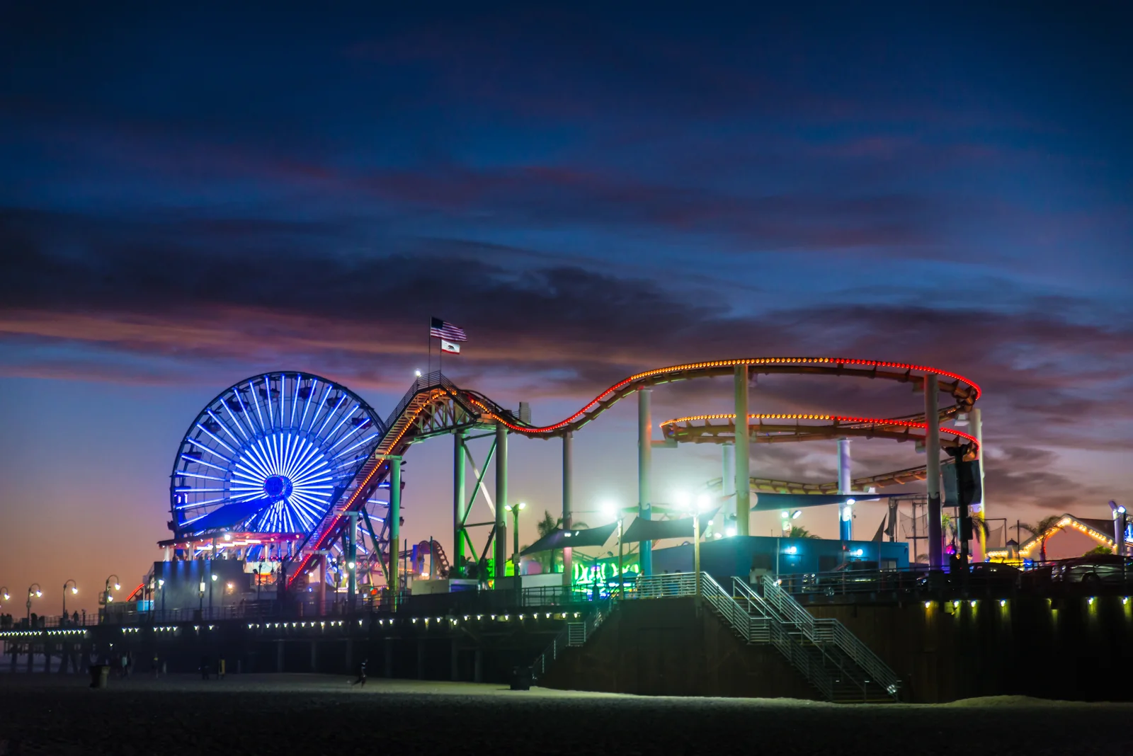 A roller coaster and Ferris wheel light up Santa Monica’s boardwalk at twilight.