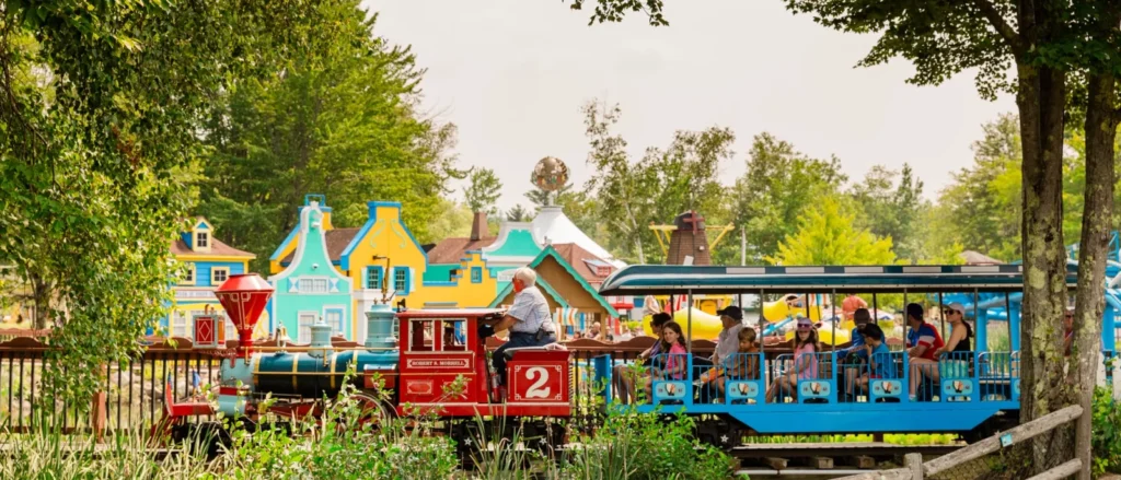 Family train ride beside colourful storybook buildings at Story Land in Glen