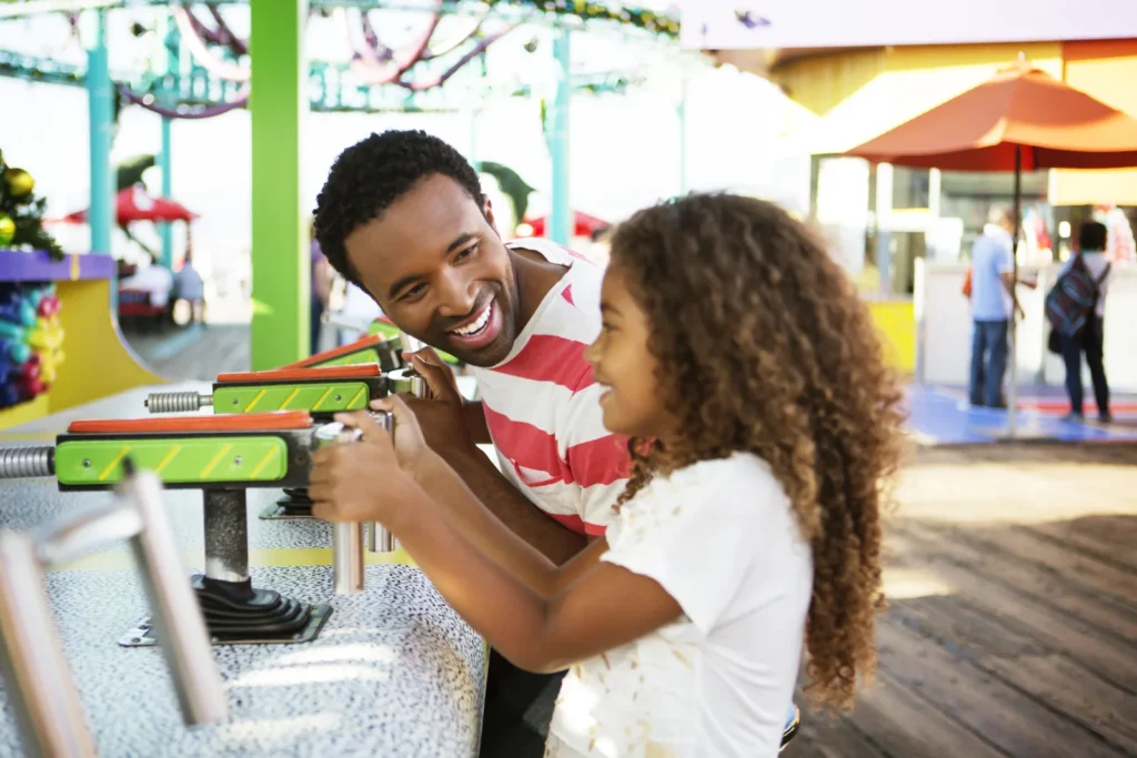 An adult and a girl enjoy a carnival game at a boardwalk.