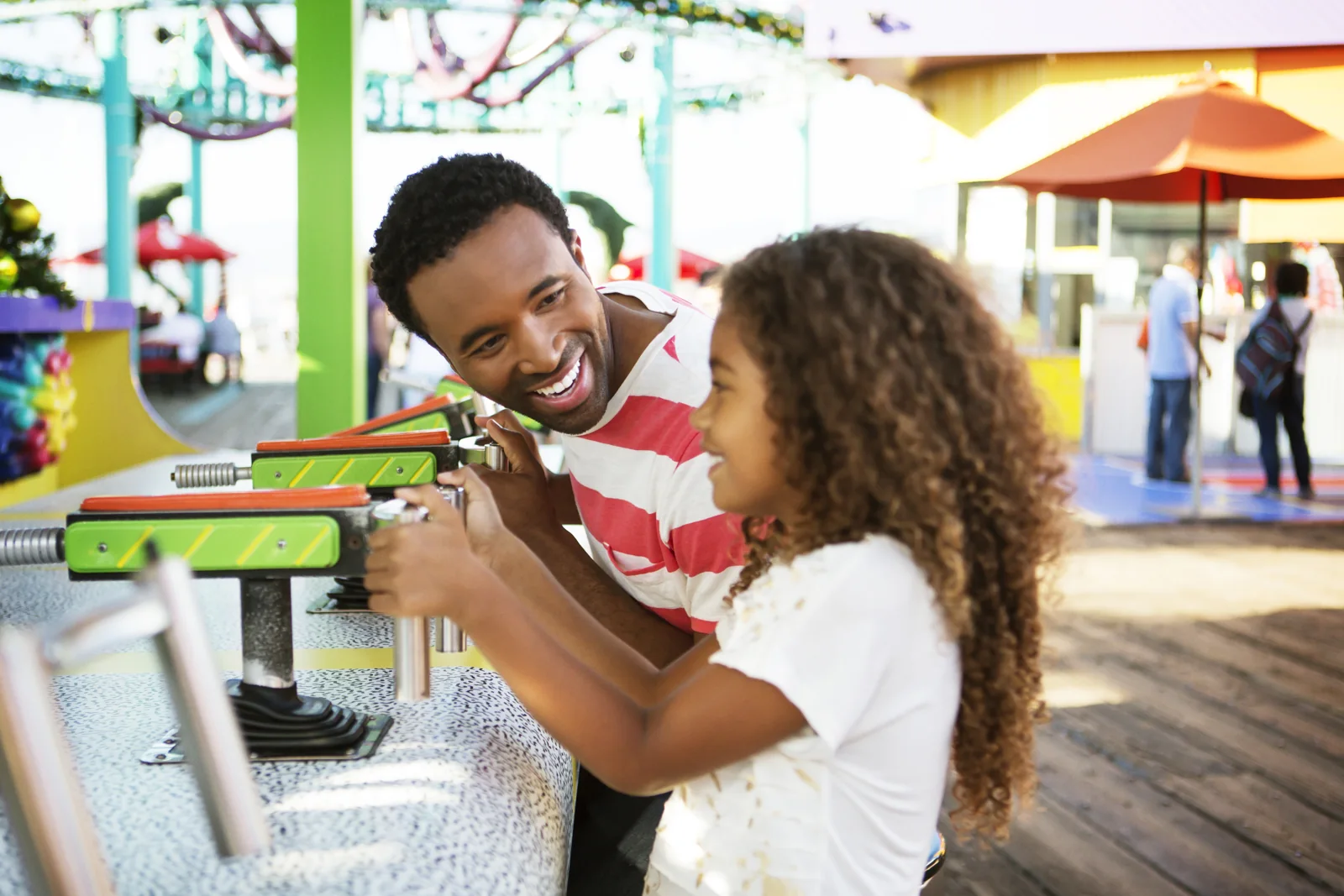 An adult and a girl enjoy a carnival game at a boardwalk.