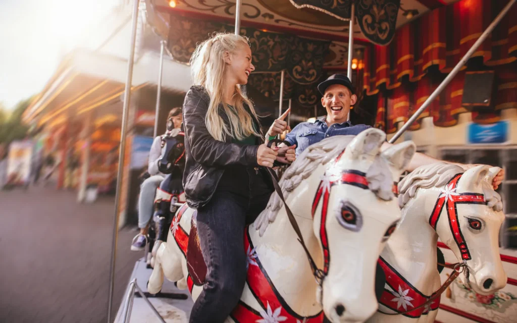 A smiling couple rides carousel horses together.