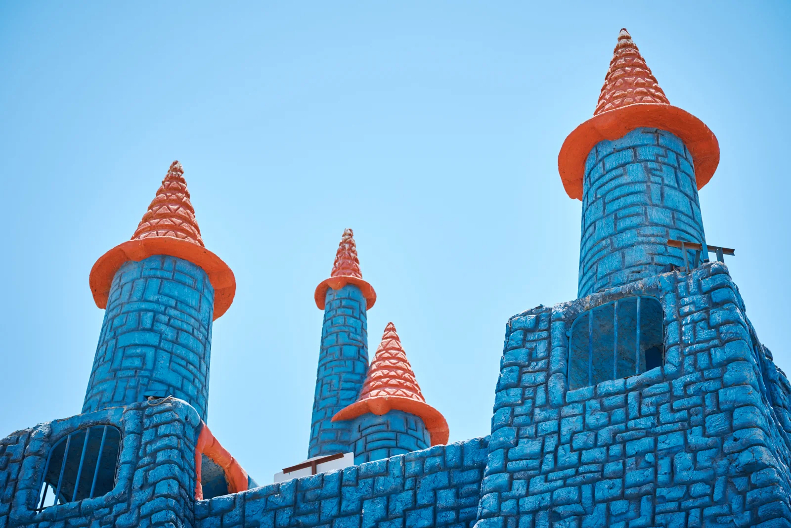 Blue castle walls rise to orange pointed towers beneath a clear sky.
