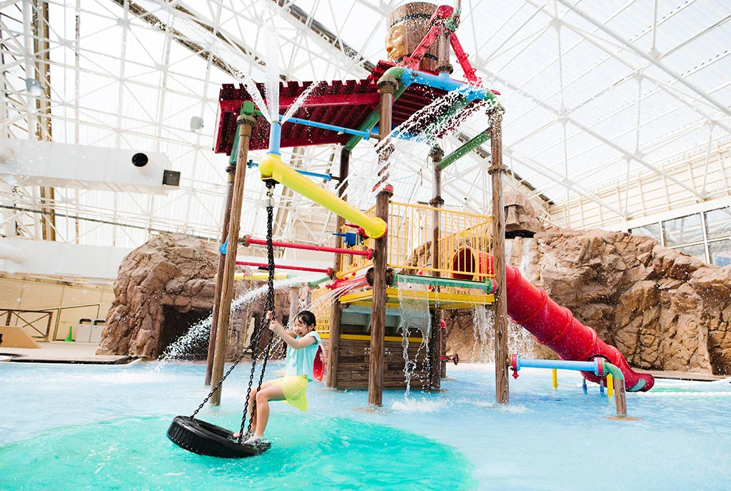 Child playing on a swing beside the indoor water structure at Tokyo Summerland
