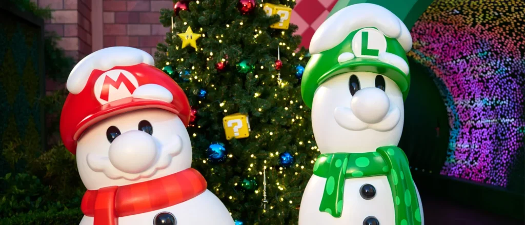 Mario and Luigi snowmen stand beside a decorated Christmas tree in SUPER NINTENDO WORLD at Universal Studios Hollywood.