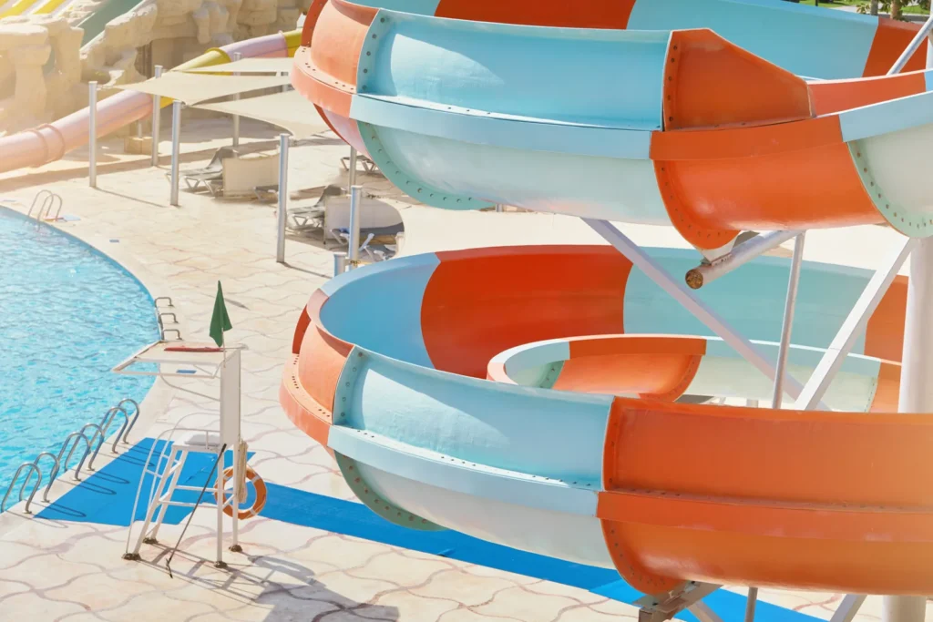Blue and orange water slides curve above a pool and sunlit deck.