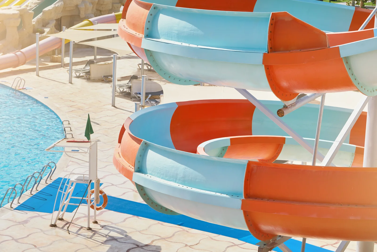 Blue and orange water slides curve above a pool and sunlit deck.