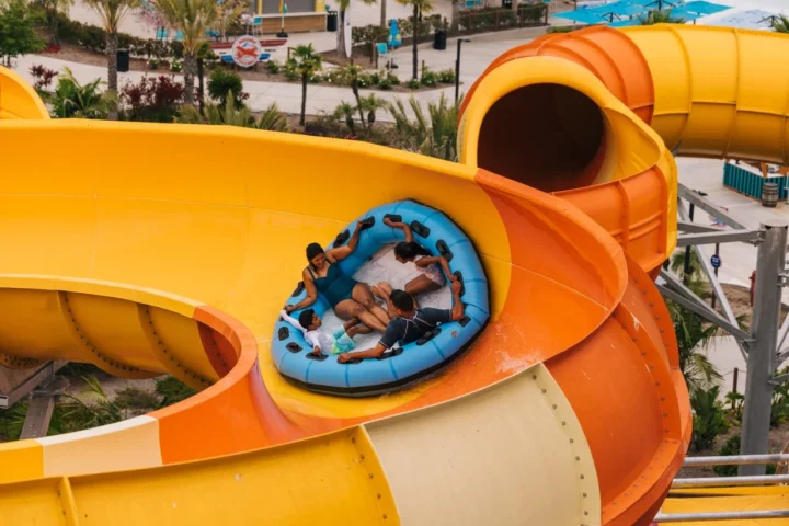 A family riding a blue raft through a water slide at Wild Rivers in Irvine